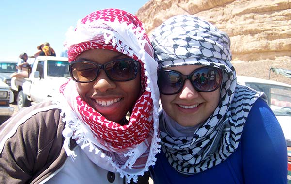 Two young women in hijabs smiling at the camera in an arid setting